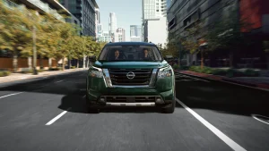 Green 2022 Nissan Pathfinder driving down the street in the city. 
