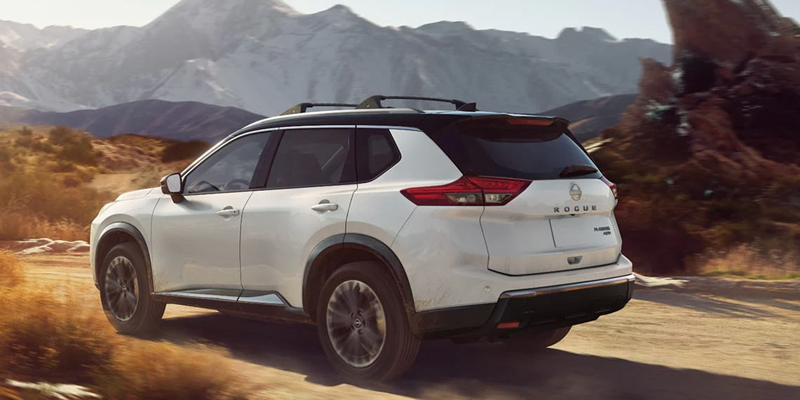 White Nissan Rogue SUV driving on a scenic mountain road with a rugged landscape background